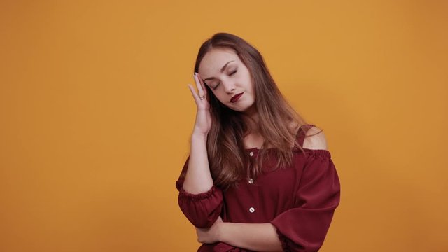 Disappointed woman in maroon dress isolated on orange background in studio keeping fingers on head, like gun. People sincere emotions, lifestyle concept.