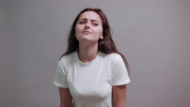 Charming caucasian brunette young woman in fashion white shirt keeping hand near ear, listening isolated on gray background in studio. People sincere emotions, lifestyle concept.