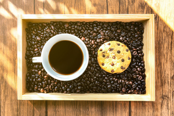 A Cup of Coffee in the Coffee Beans with Cookie on the Wooden Plate at Morning Time