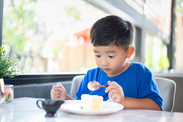 Asian boy eating cake in bakery shop or cafe.