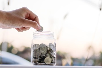 Hand hold and put coins in piggy bank on wooden table with natural background, growing and savings money concept