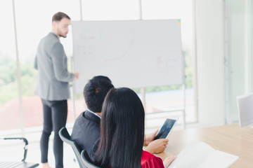 Young businessmen are explaining graphs and statistics on a whiteboard. The managers and employees of the company attending the meeting.
