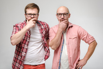 Two serious, pensive men in glasses, hold hands on their faces and stare at the camera in...