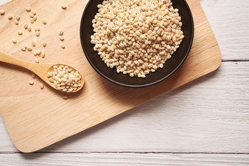 Pearl barley grain in black ceramic bowl and wooden spoon on wooden plate and wooden background ,Top view perspective