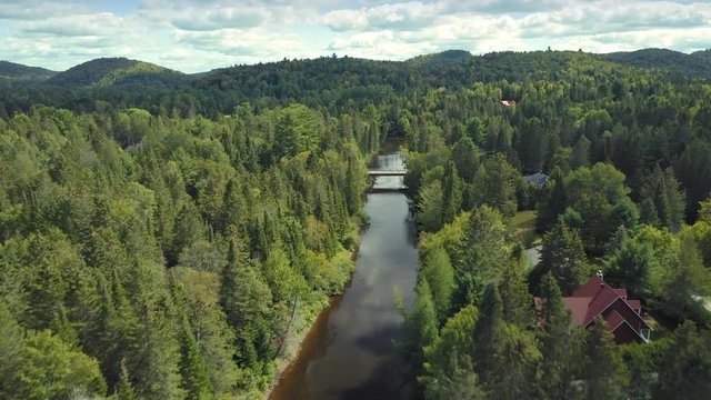 Aerial: Flying down a calm mirror river with forest. Val David, Quebec, Canada