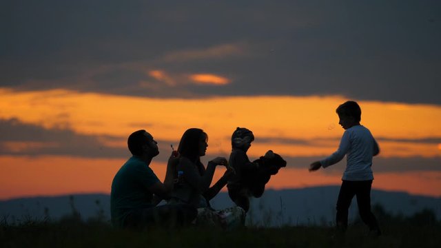 Happy family sunset silhouette portrait, parents blow bubbles and children play, magical moments in nature