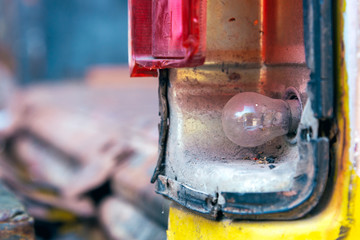 Head bulb in a broken headlight of dirty abandoned car.