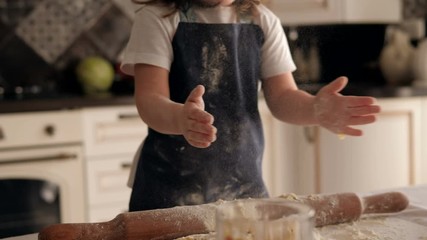 Close-up of a little charming girl smeared with flour claps her hands, she takes the flour in her hands and claps hard, the flour flies around. Slow motion. - Powered by Adobe