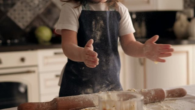 Close-up of a little charming girl smeared with flour claps her hands, she takes the flour in her hands and claps hard, the flour flies around. Slow motion.