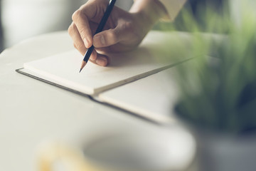 Close up of male hand writing with pencil on the book. Businessman working with data information in the office.