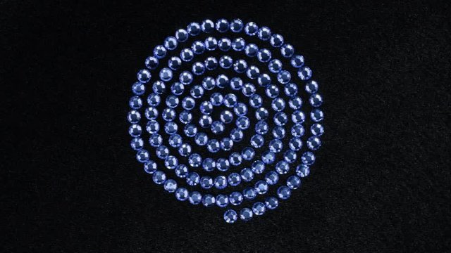 Rotation of the rhinestones laid out in a spiral shape lying on black fabric. Top view.