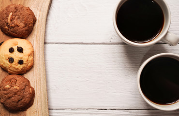 top view of two cups of hot americano or espresso coffee with chocolate chip and almond cookie on ceramic plate on white wooden background ,breakfast in minimal concept with copy space