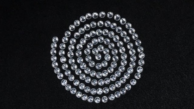 Rotation of the rhinestones laid out in a spiral shape lying on black fabric. Top view.