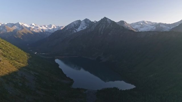 Drone panning above lake basin of Multa lake belted with snowy ridge on sunset