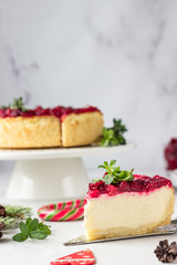 Classical New York cheesecake with cranberry sauce, mint and rosemary, light grey stone background. Festive Christmas decoration.