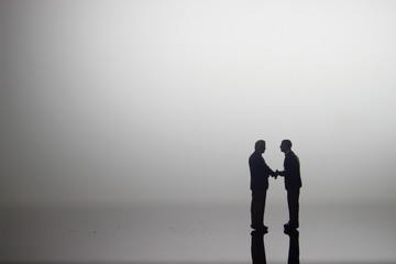 Dramatic Lighting, Simple Illustration Photo for Silhouette Two Miniature Figure Man Toy Handshaking for Business Agreement between they team 