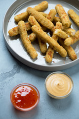 Close-up of breaded chicken sticks on a grey plate with dipping sauces, vertical shot