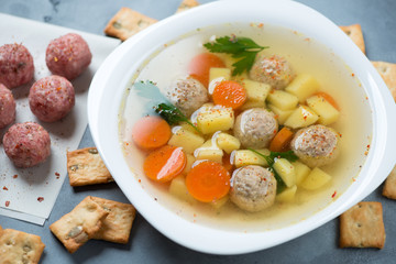 Close-up of soup with meatballs, potato, carrot and parsley served in a white plate, studio shot