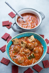 Tomato soup with meatballs, vermicelli and crackers, vertical shot over light-blue stone background