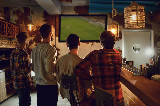 A Group Of People Watching Tv Football In A Sports Bar.