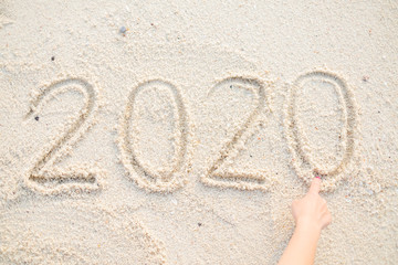 Hand writing 2020 Happy new year message on the sand beach.
