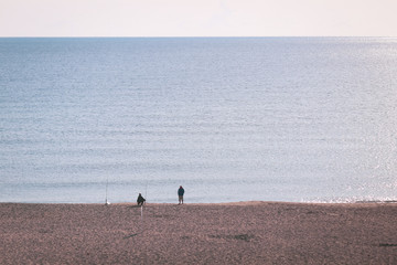 Fototapeta na wymiar Silhouettes of two fishermen on the beach during a clear sunrise on the seaside