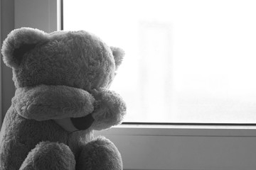 A soft toy bear cries sitting on a windowsill. There are noises in the photo, because the photo is dark. black and white photo