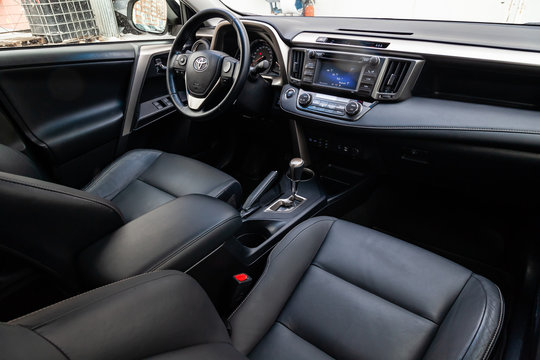The interior of the car Toyota Rav4 with a view of the steering wheel, dashboard, seats and multimedia system with black leather trim and the letter-shaped emblem