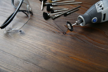 rotary tool with a nozzle for cleaning something on a wooden background. backdrop for repair and cleaning workshop: protective glasses, electric rotary tool and nozzles