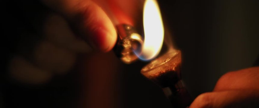 A person lighting up a glass bong of weed, the process of smoking medical marijuana. Dark room at night, close up, shallow depth of field, beautiful bokeh, cinematic shot with BMPCC 4K