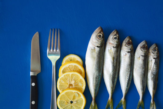 Fresh horse mackerel fish on a blue background, lemon, fork, knife.Top view on the table Place for text. Healthy food concept, mediterranean diet.