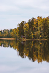 Fototapeta na wymiar Autumn forest and lake reflection house in woods landscape in Finland Travel serene scenic view scandinavian wilderness nature