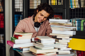 Intellectual man reading a book sitting in library in front of bookshelves.