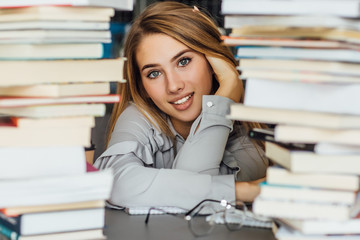 Beautiful young college student woman in a library, posing with glasses and books.