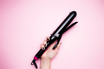 Naklejka premium Female hand holds a hair curler in black on a pink isolated background close-up.