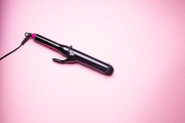 Closeup black hair curler on pink isolated background.