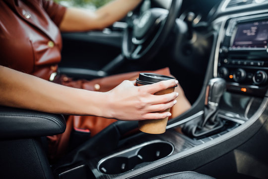 Young woman hands with coffee to go driving her car, close up photo.
