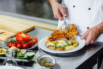 Chef serving a dish of prepared potatoes with herbs and fish on white plate at the restaurant's cuisine, close-up. Cook pours a tomato sauce on dish.