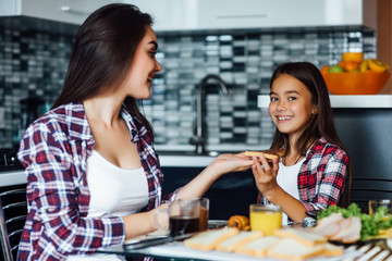 Happy girls in the kitchen. Mother and pretty child daughter are having breakfast with sandwich.