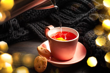 A cup of tea with lemon. Water is poured from an electric kettle. Bokeh lights for Christmas mood