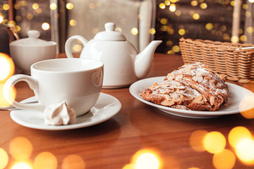 Obraz na płótnie Canvas White cup, tea pot and croissant on table in cafe