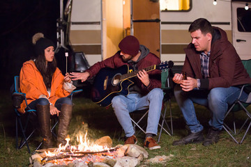 Campers playing on guitar and roasting marshmallows