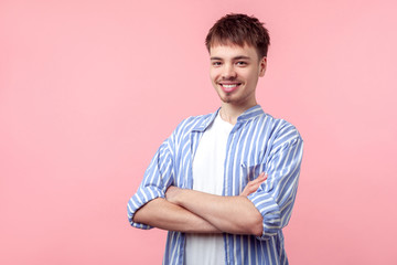 Fototapeta premium Portrait of young successful brown-haired man with small beard and mustache in casual shirt standing confident with arms crossed, smiling at camera. indoor studio shot isolated on pink background