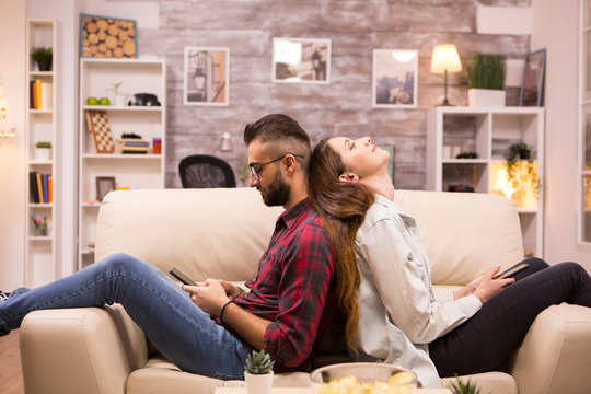 Upset Couple Sitting Back To Back On Sofa In Living Room