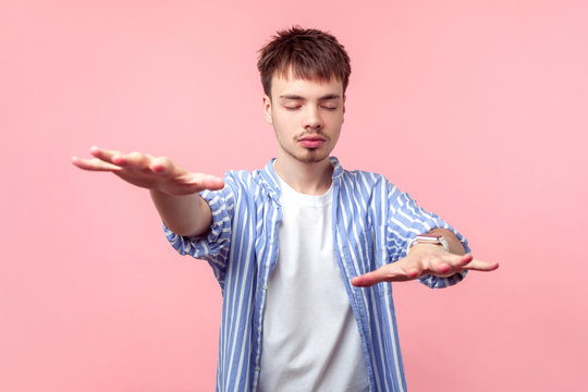 Portrait of disoriented blind brown-haired man with small beard and mustache in casual shirt walking with closed eyes, stretching hands to find road. indoor studio shot isolated on pink background