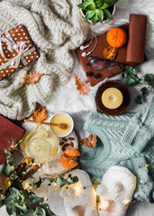 Cozy winter autumn things. Home cozy still life - slippers, knitted sweater, plaid, green tea with honey, tangerines, dry leaves, books, garland, gift box  light background. Autumn winter relax mood