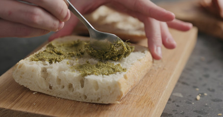 man spread pesto on ciabatta slice on oak board