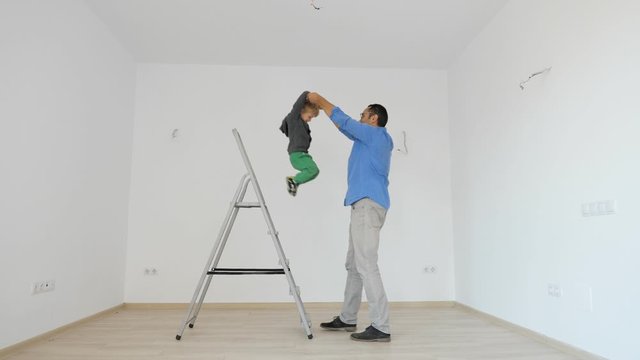 Father hold child hands and help him to jump down from ladder
