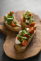 Bruschetta with mozzarella, cherry tomatoes and pesto on olive board