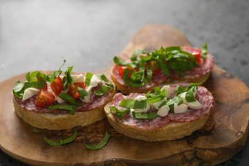 Bruschetta with mozzarella, cherry tomatoes and salame on olive board